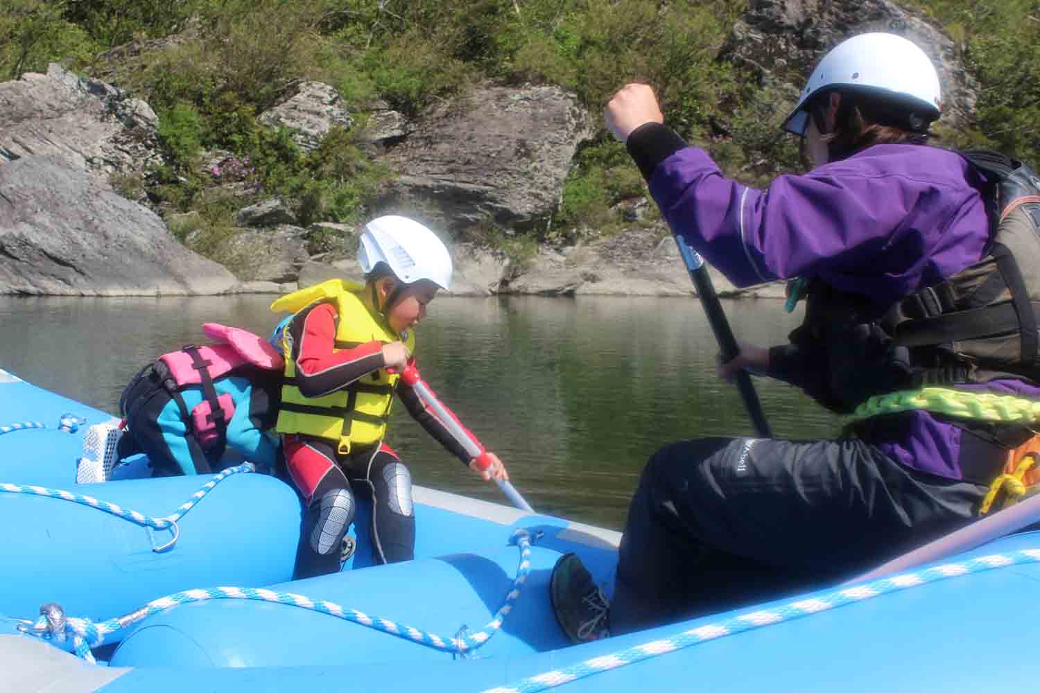 幼い子供を吉野川でラフティングボートに乗せてゆっくり漕ぎ方を教える親子の写真
